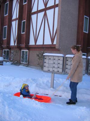 Katie pulls Noah on the sidewalk on his sled.