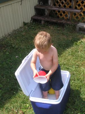 Noah plays in the water in the blue cooler.