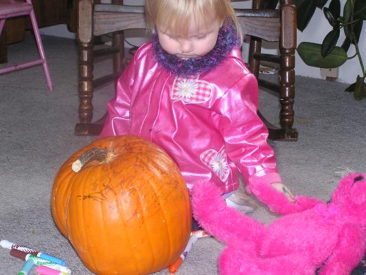 Sarah, in her hot pink jacket, plays wiht a hotpink bear and a pumpkin.