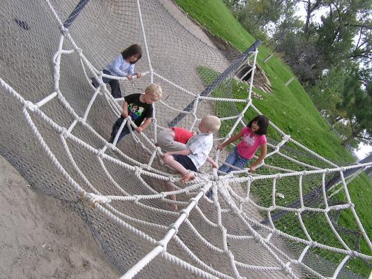 The kids play in the spider web at the playground.