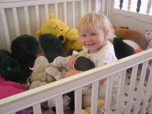 Sarah is playing in her crib with stuffed toys.