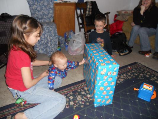 Andrea helps Joshua open another gift. It is from Mike and Cindy and them. 