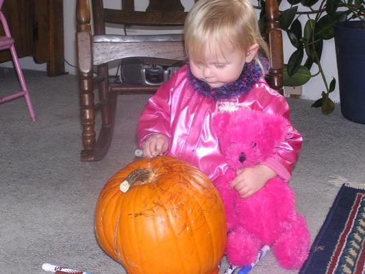 Sarah and a pink bear color a pumpkin.