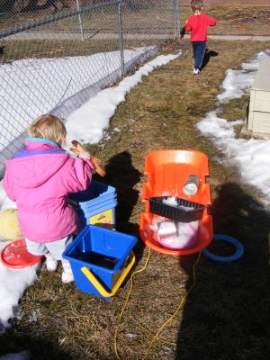 Sarah plays with the sand toys in the snow. Noah runs around.