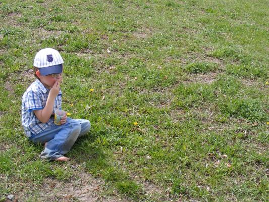 Noah sits in the grass with his new striped baseball hat.