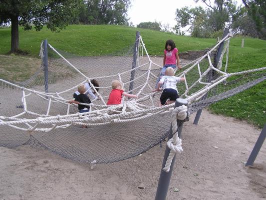 The kids play in the spider web at the playground.
