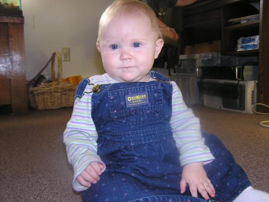 Sarah sits in her overalls dress.