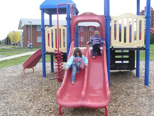 Andrea and Noah play on slides at the park.