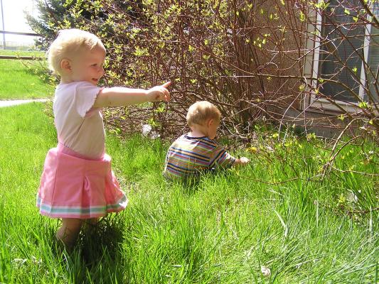 Sarah and Noah play with the cotton in the grass. 
Sarah is pointing at the dandilions.