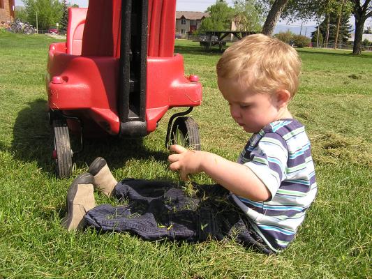 Noah burries his legs in grass clippings.
