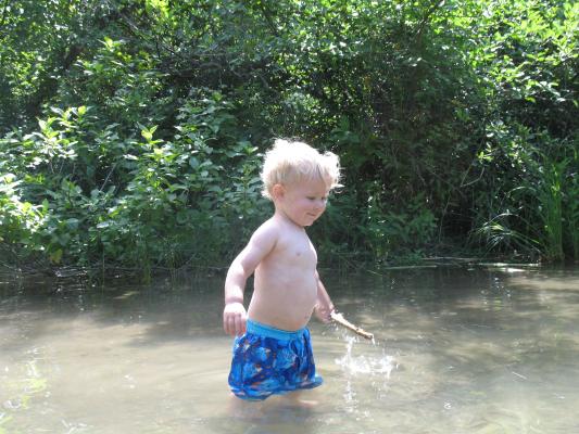 Noah plays with a stick in the water.