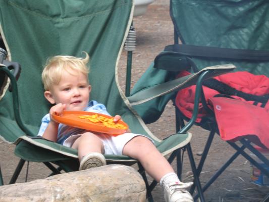 Noah sitting in a green camp chair eating goldfish crackers off an orange frisbee.