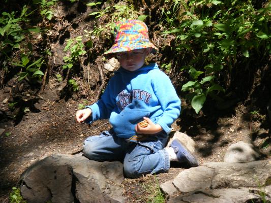 Noah plays in a creek. He hold tightly to those sandwich cookies.
