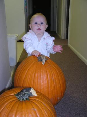 Sarah stands up with the help of a big pumpkin.