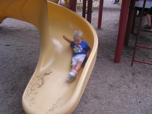 Noah goes down a slide at the park.