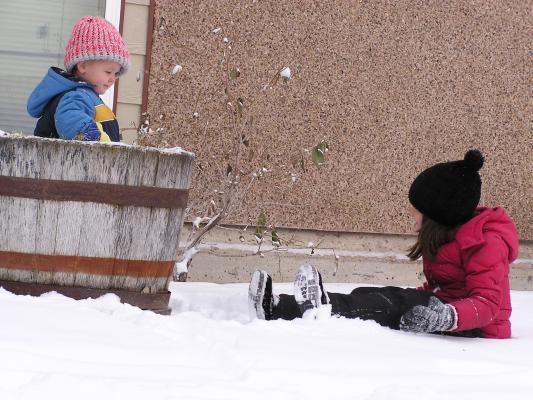 Andrea shows Noah that she can sit in the snow because she has snow pants.