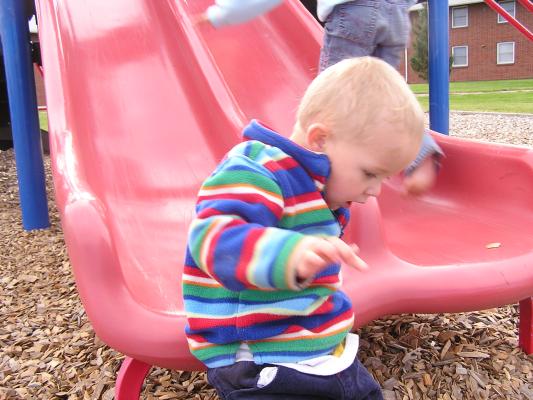 Noah slides off the slide at the park.