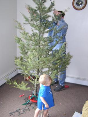 Noah helps put lights on the tree. David and Noah go around and around the tree.