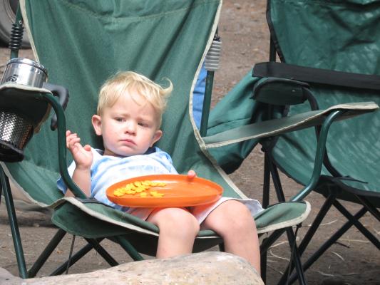 Noah sits on a green camp chair eating goldfish crackers on a frisbee.