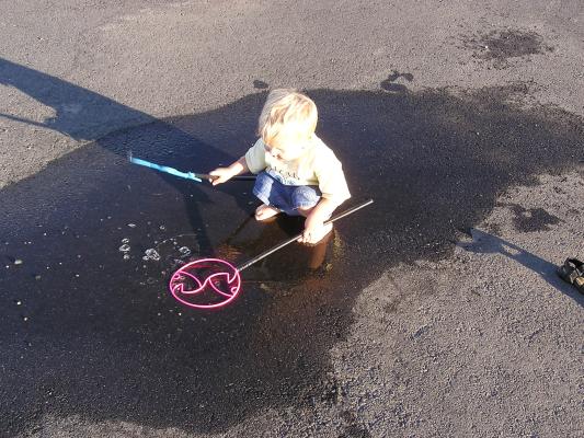 Noah plays with the bubble wands in a mud puddle.
