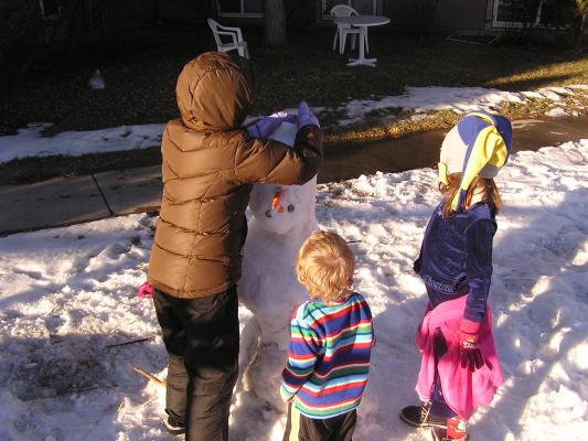 Malia is building a snowman as Noah and Andrea look on .